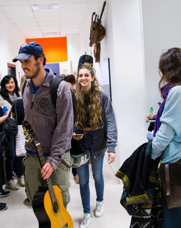 Studenti e visitatori accedono alla Scuola e Accademia di Musica Cluster per l’Open Day, accolti in un ambiente informale e sorridente, con chitarre in mano e staff presente
