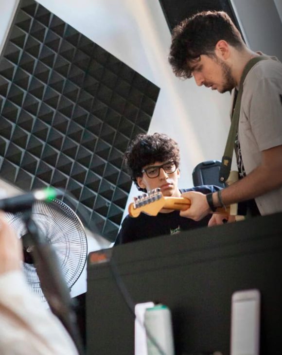 Studente della Scuola e Accademia di Musica Cluster osserva attentamente il docente durante una lezione individuale di chitarra elettrica in un’aula insonorizzata